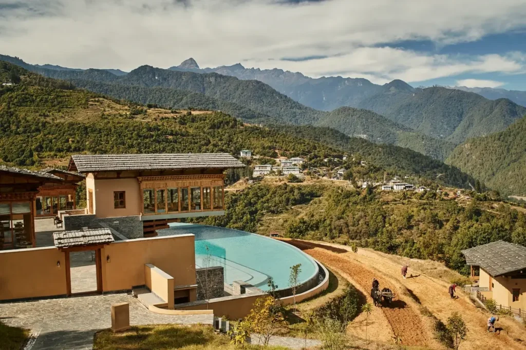 Earth-toned lodge buildings and a curved outdoor pool overlook terraced fields and a mountainous valley.