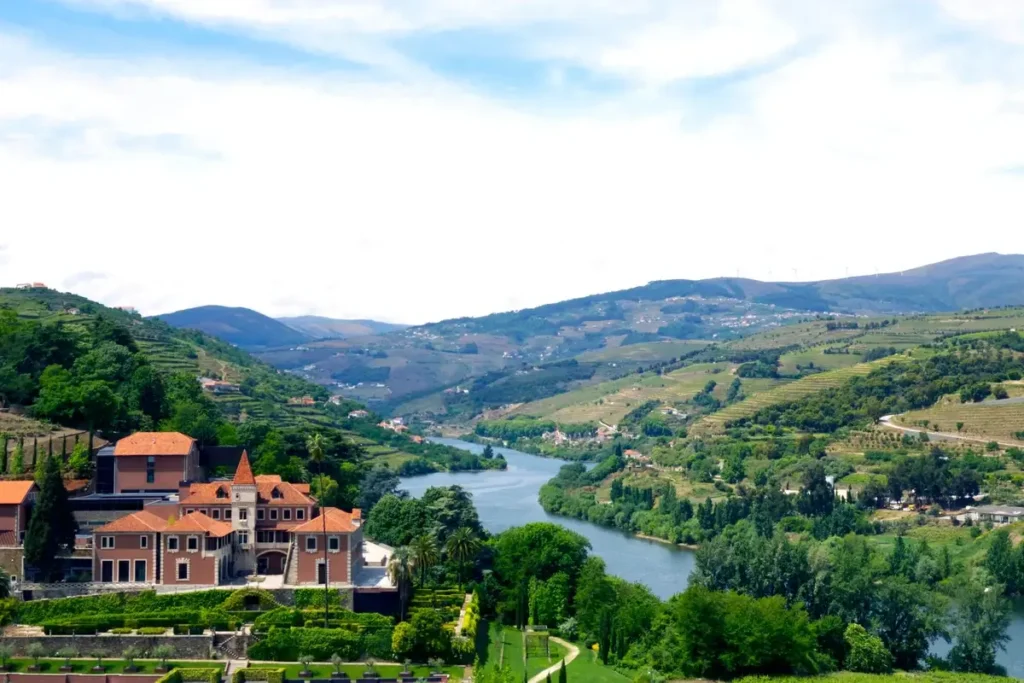Red-roofed hotel buildings sit below wooded slopes beside the winding Douro River and vineyard-covered hills.
