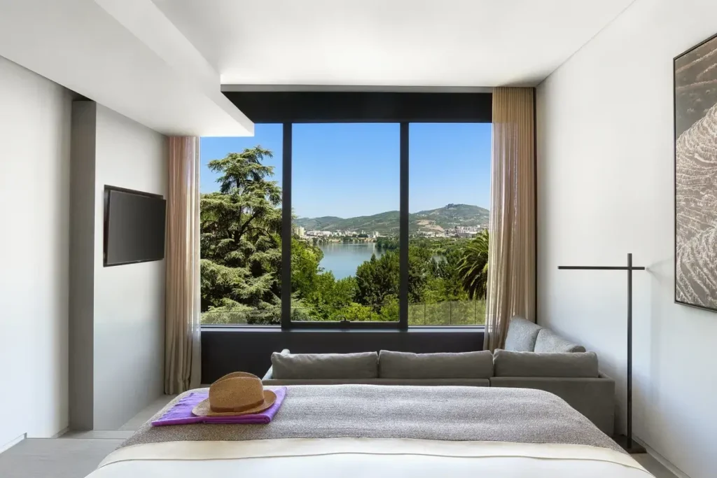 A bed and gray sofa face a large window framing trees, the Douro River, and distant hills.