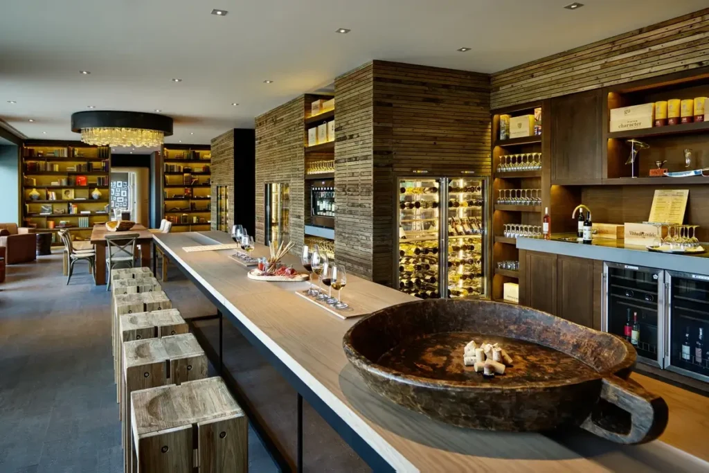 A long tasting counter with stools and wine glasses runs between wooden shelves and illuminated wine cabinets.