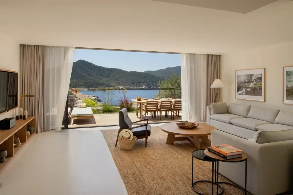Pale sofas and low tables in a residence opening onto a dining terrace with bay views at Six Senses Ibiza