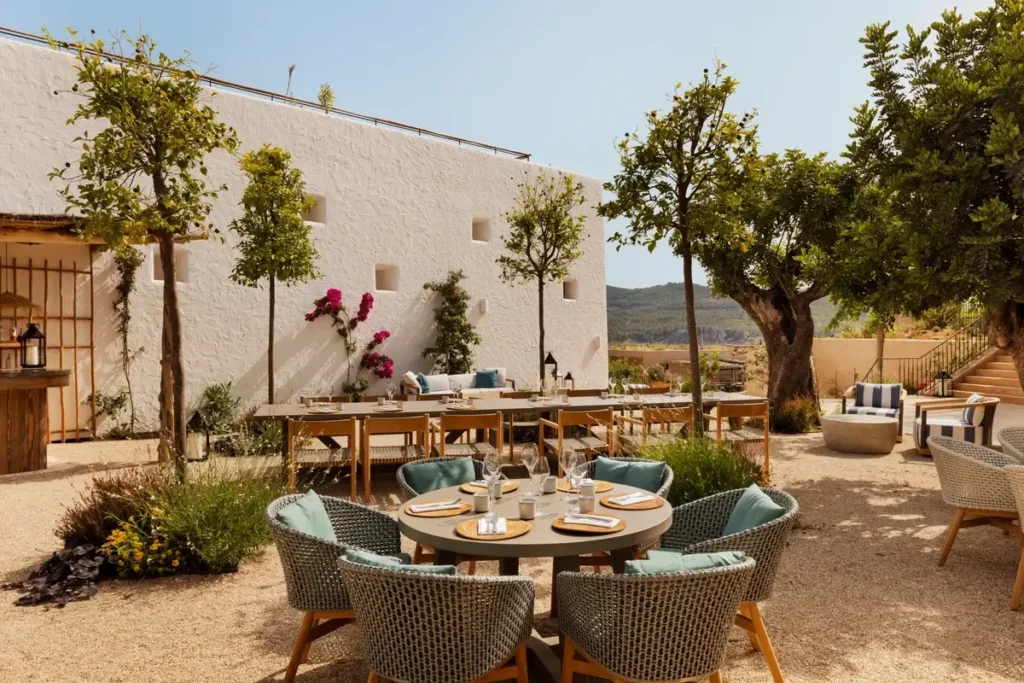 Set dining tables, woven chairs, and trees in the Orchard courtyard at Six Senses Ibiza