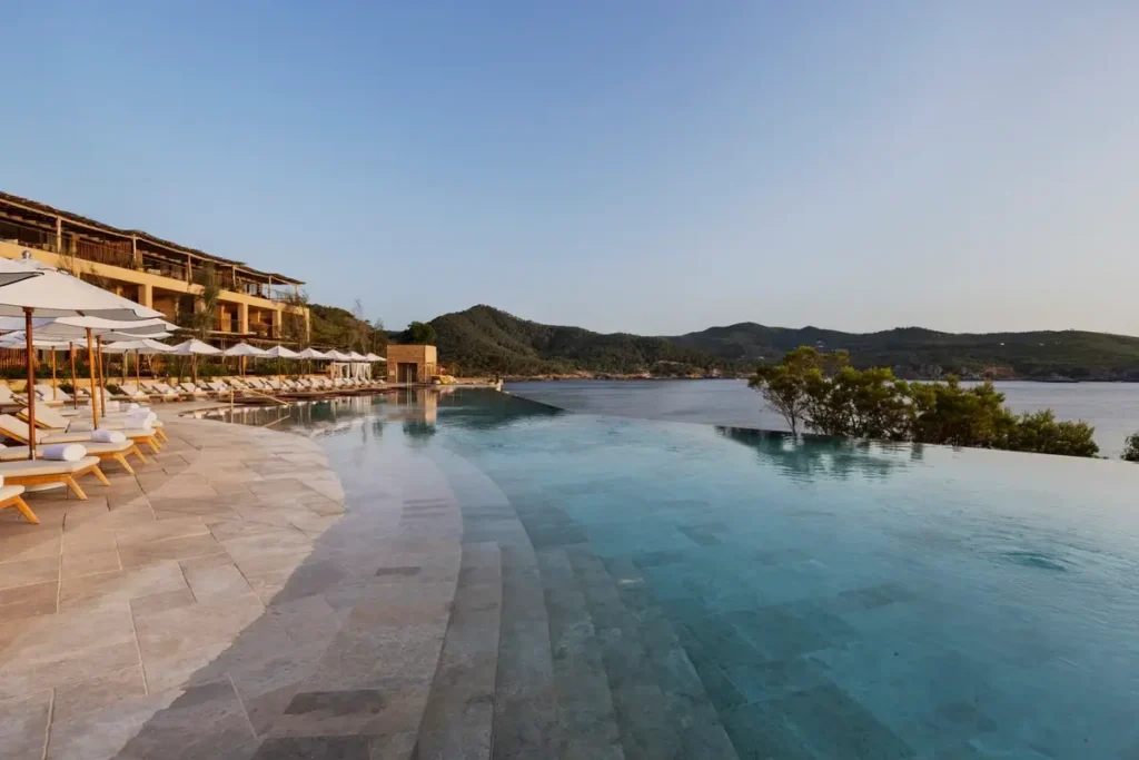Wide infinity pool beside rows of shaded loungers overlooking the bay at Six Senses Ibiza