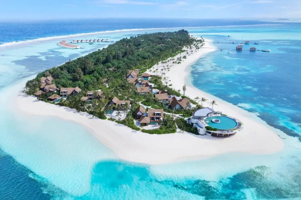 A broad white-sand beach wraps around a palm-covered island surrounded by turquoise lagoon water.