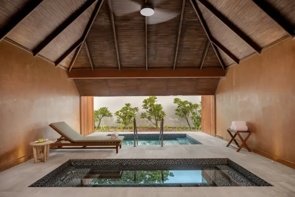 Small tiled pools and a lounger sit beneath a pitched timber roof in a sheltered spa pavilion.