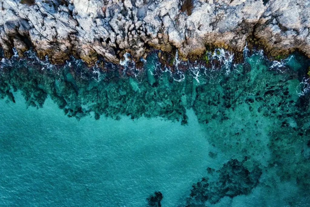 Clear turquoise water meets pale coastal rocks, with submerged formations visible below the surface.