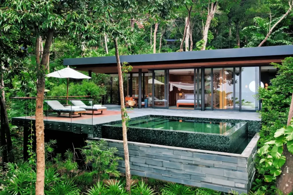 A glass-fronted villa and private pool sit on an elevated deck surrounded by dense tropical trees.