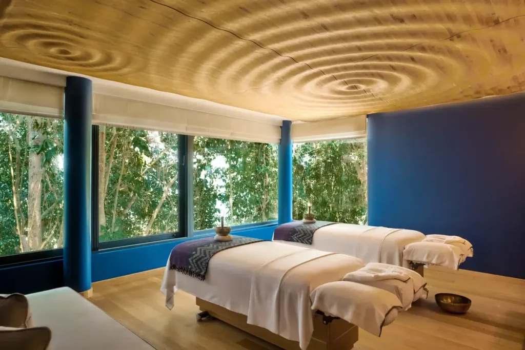 Two treatment beds sit beside forest-facing windows beneath a golden ceiling patterned with concentric circles.