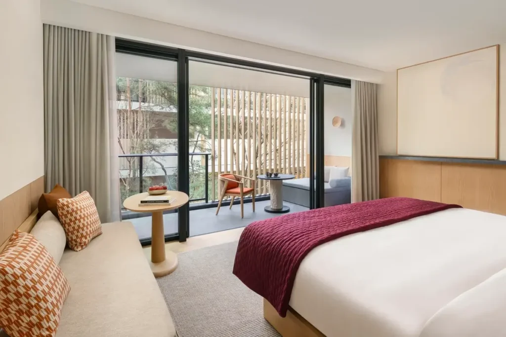 King bed with a burgundy throw, sofa, and glass doors facing a planted terrace at Six Senses Kyoto
