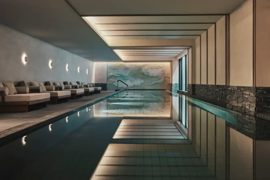 Long indoor pool with lounge chairs, ceiling beams, and a mural at the far end at Six Senses Kyoto