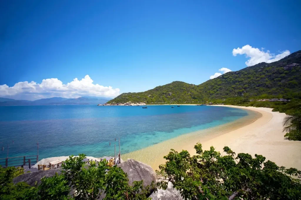 Sweeping sandy beach beside clear blue water and forested hills at Six Senses Ninh Van Bay