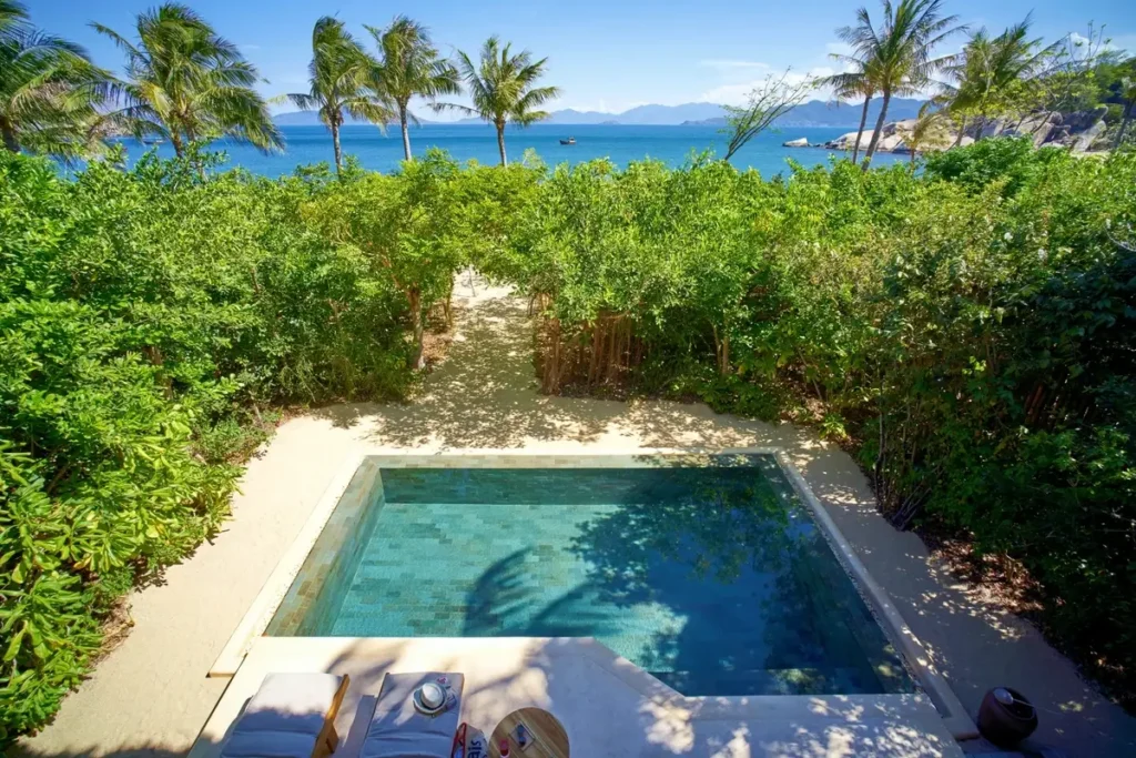 Rectangular private pool surrounded by dense hedges, with palms and the sea beyond at Six Senses Ninh Van Bay