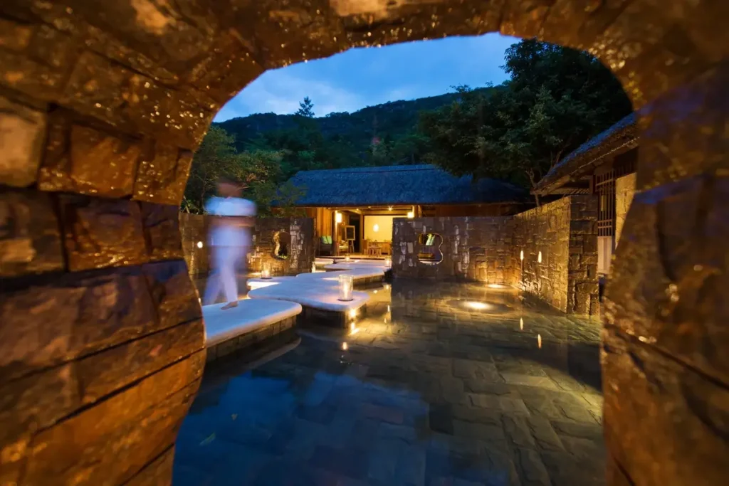 Stone archway framing a softly lit spa courtyard and reception building at Six Senses Ninh Van Bay