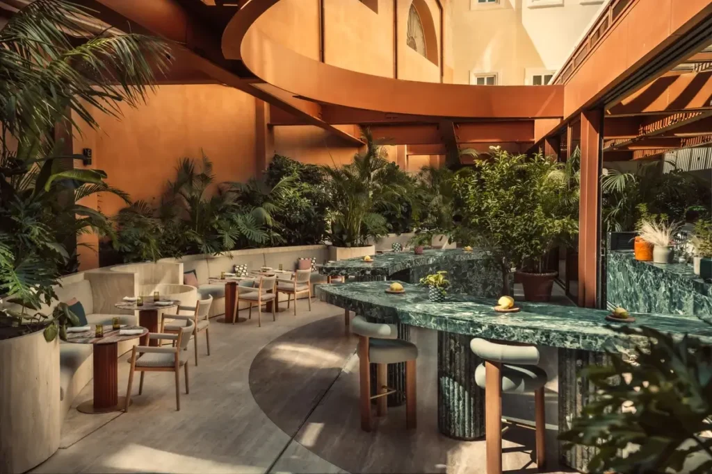 Curved green stone bar surrounded by stools, dining tables, and tropical planting at Six Senses Rome