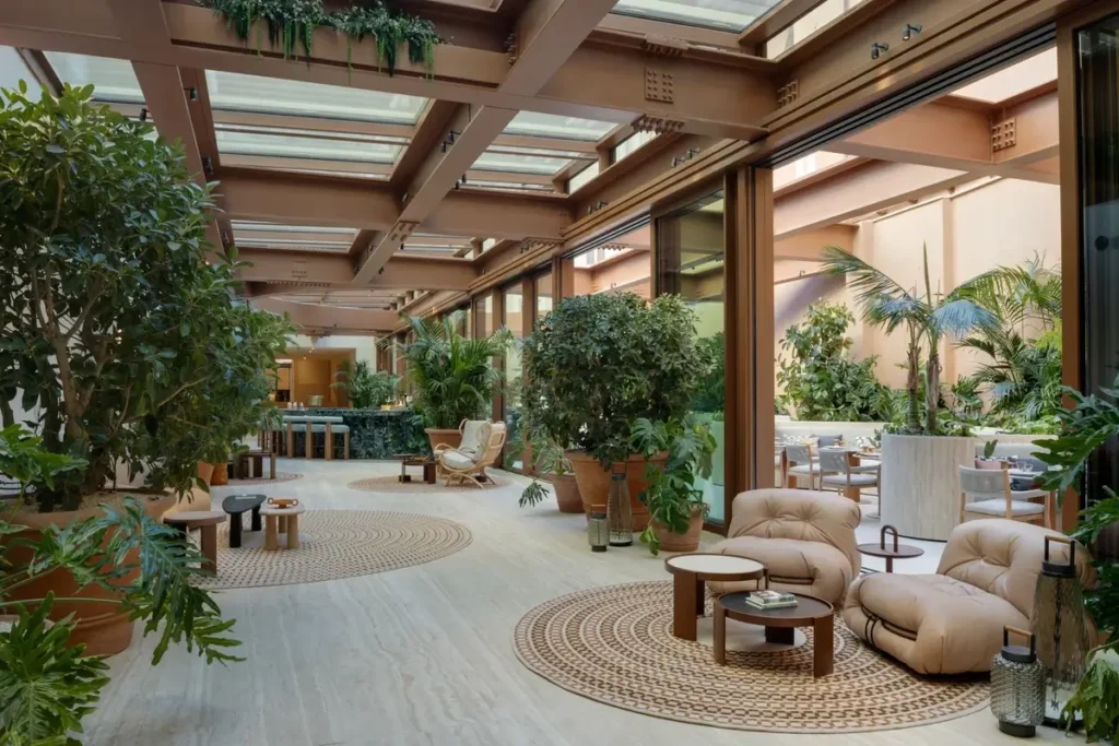 Rounded lounge chairs and low tables among large plants beneath a glazed ceiling at Six Senses Rome