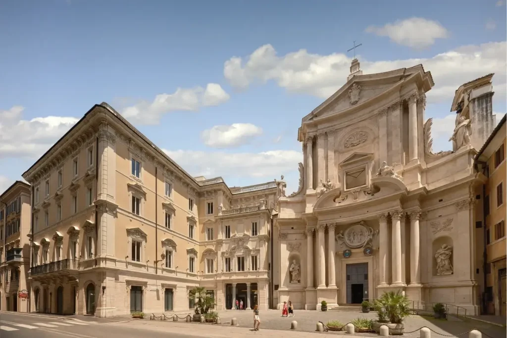 Pale historic facade of Six Senses Rome beside the ornate front of San Marcello al Corso church
