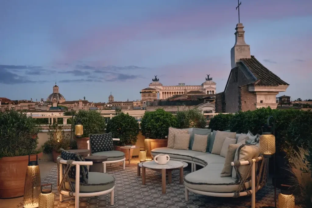 Cushioned rooftop seating, potted plants, and lanterns overlooking Rome at dusk from NOTOS at Six Senses Rome