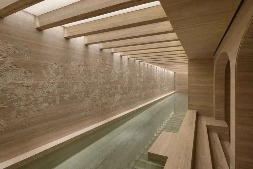 Long indoor bathing pool beside a carved stone wall beneath ceiling beams at Six Senses Rome
