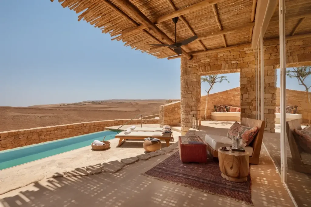 A private pool runs beside a stone terrace with loungers and shaded seating overlooking the desert.