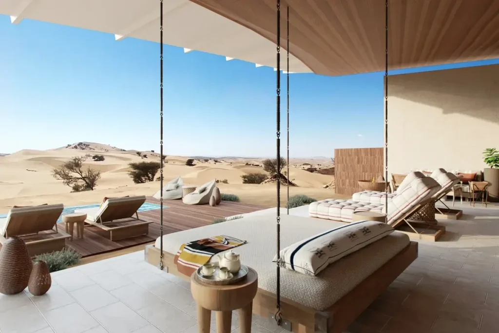 Shaded villa terrace with a suspended daybed, loungers, and a private pool facing sand dunes