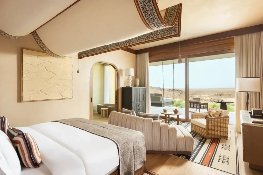 King bed and pale seating facing full-height windows and a desert-view terrace in a Wadi King Room