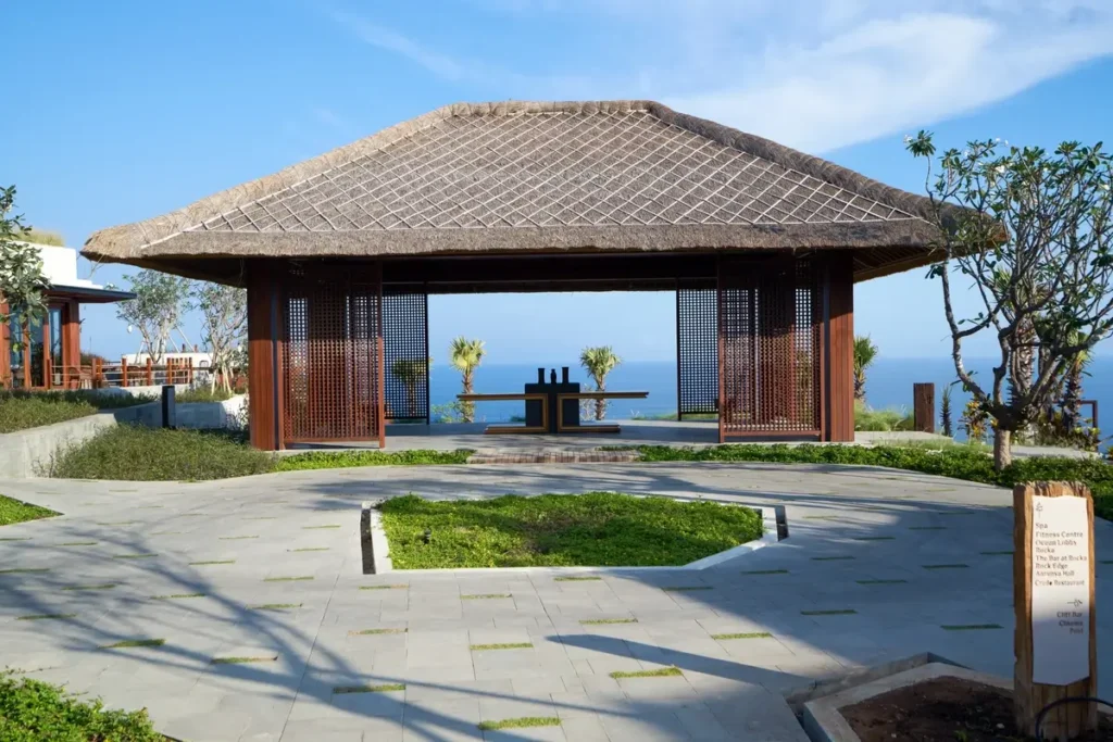 An open-sided pavilion with a tiled roof faces the sea across a lawn and a shallow reflecting pool.