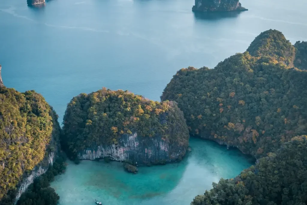 Forested limestone islands rise from turquoise coves and blue water in an aerial view of Phang Nga Bay.