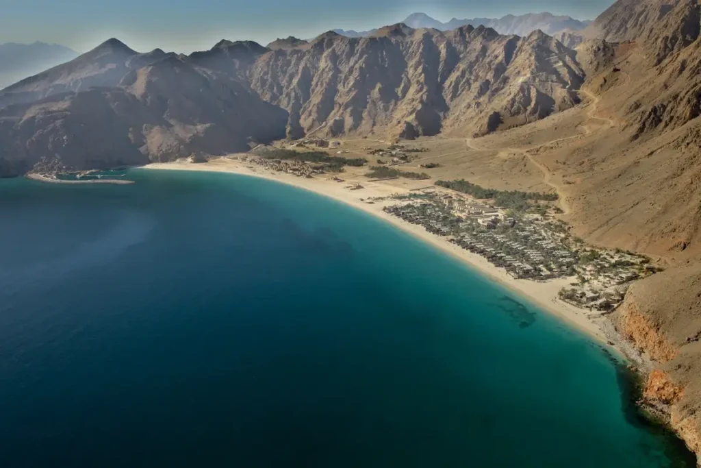 Aerial view of a broad sandy bay and resort beneath rugged mountains at Six Senses Zighy Bay