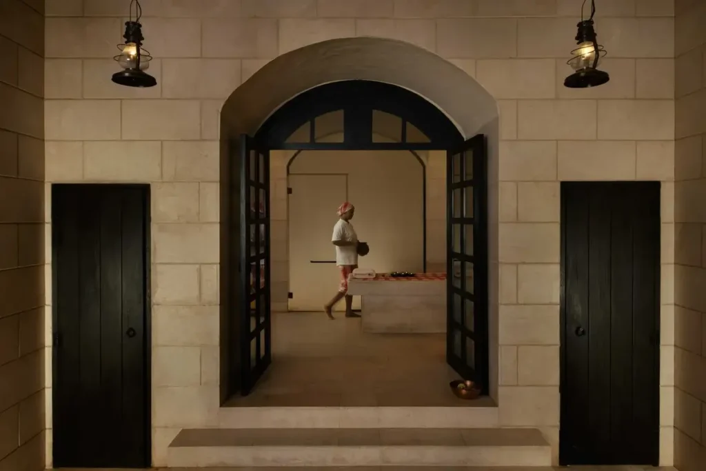 Stone arch and open dark doors framing a person inside the hammam at Six Senses Zighy Bay