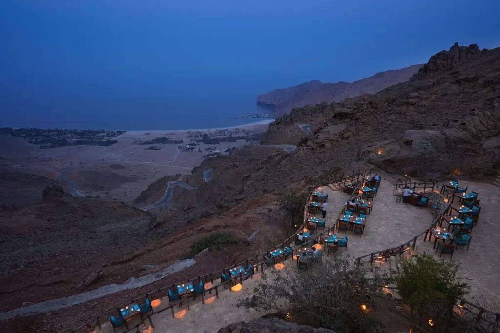 Illuminated dining tables on a mountainside terrace overlooking the bay at Sense on the Edge